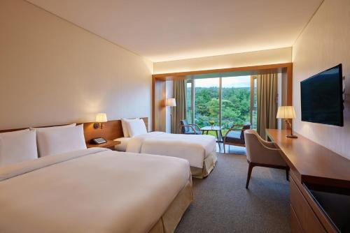 a hotel room with two beds and a desk at WE Hotel Jeju in Seogwipo