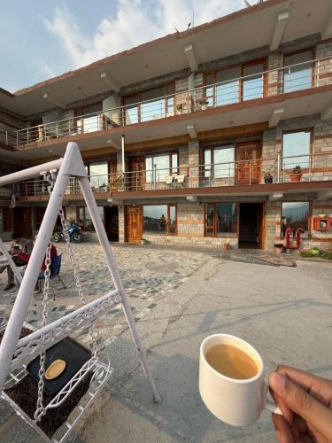 a person holding a cup of coffee in front of a building at Cedar Valley Retreat in Jagatsukh