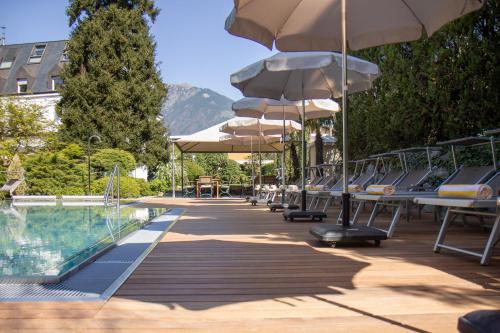 a pool with chairs and umbrellas next to a swimming pool at Hotel Sonnenhof in Merano