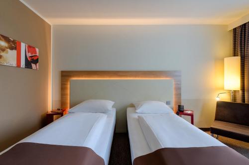 a hotel room with two beds and a chair at Mercure Hotel Stuttgart Airport Messe in Stuttgart