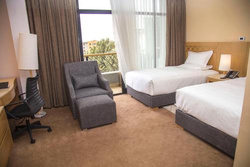 a hotel room with two beds and a chair and a window at Vamos Addis Hotel in Addis Ababa
