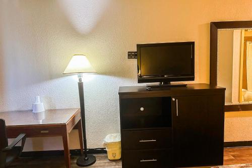 a room with a tv on a dresser with a desk and a lamp at Jackson Hotel And Convention Center in Jackson