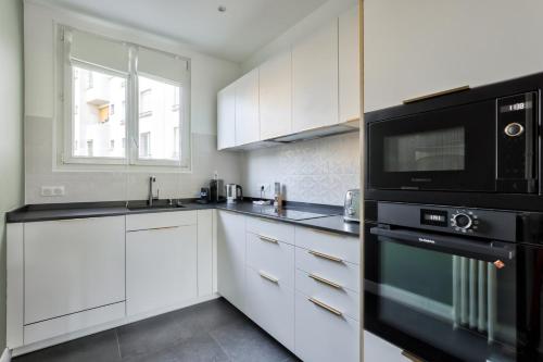 La cuisine est équipée de placards blancs et d'un four micro-ondes noir. dans l'établissement GuestReady - Charming Stay in Montsouris, à Paris