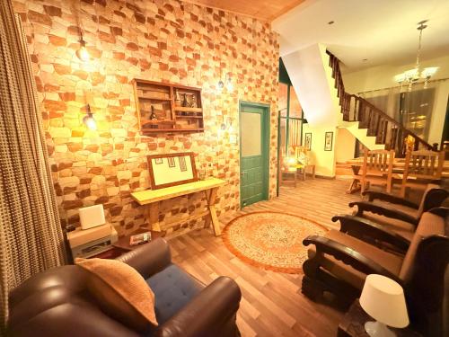 a living room with leather furniture and a stone wall at Frogs BNB Aviator's Bungalow in Dharmsala