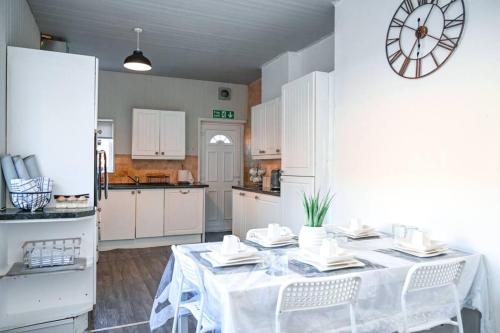 une cuisine blanche avec une table et une horloge murale dans l'établissement Humble Home NE - Short & Long stay or Contractors, à Gateshead