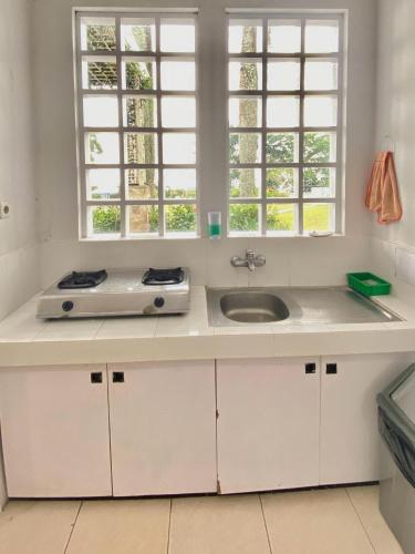 a white kitchen with a sink and two windows at In Villa Garden Resort in Batu