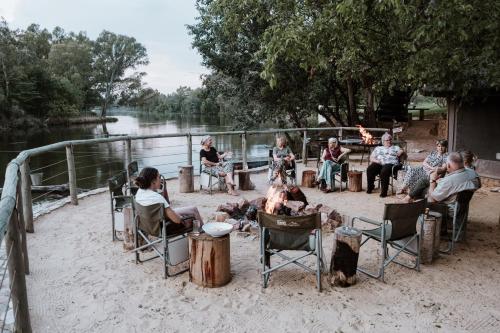 a group of people sitting around a fire near a river at Breathe River Retreat in Parys