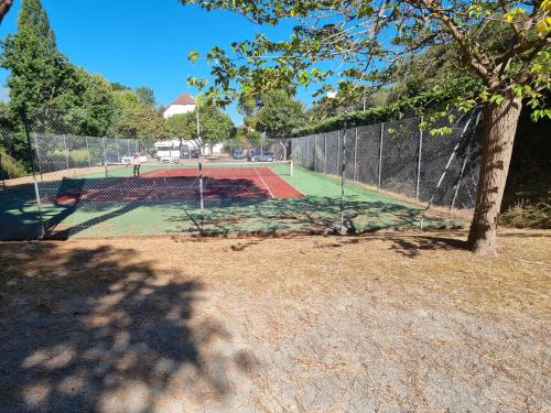 un court de tennis derrière une clôture avec un arbre dans l'établissement Les Dryades 4 pax appartement, à La Baule