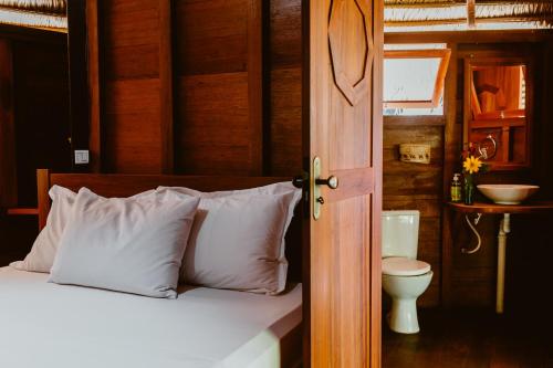a bedroom with a bed with white pillows and a toilet at Villa Arapiuns - 6 Bangalôs na Floresta in Santarém
