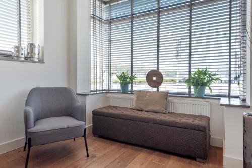 a chair and a couch in a room with windows at Wijkiki Surf House in Wijk aan Zee