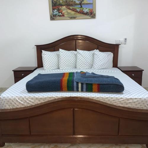 a bed with a wooden frame with a rainbow blanket on it at Park Springs Hotel in Cape Coast