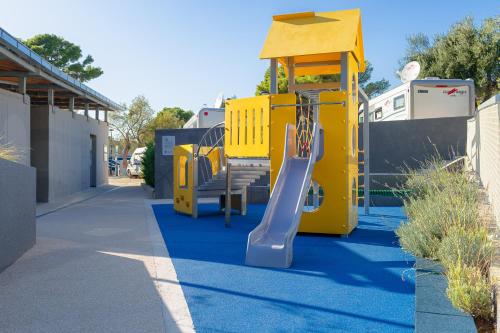 a yellow playground with a slide on a sidewalk at Medora Orbis Camping Pitches in Podgora