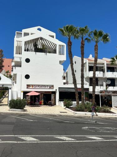a white building with palm trees in front of a street at Apt In Colina 2, Los Cristianos K105 in El Guincho