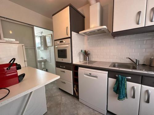 une cuisine avec des armoires blanches, un évier et un réfrigérateur dans l'établissement Le Cottage de Quettehou, à Quettehou