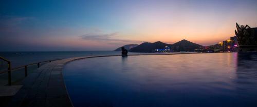 a person standing next to a swimming pool at sunset at Harman Resort Hotel Sanya in Sanya