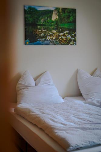 a bed with white sheets and pillows under a painting at Kleiner Urlaub in Beuron