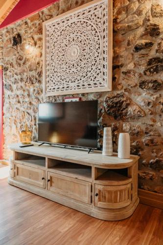 a television on a wooden entertainment center in a room with a stone wall at La Casina de Maxa in Suares