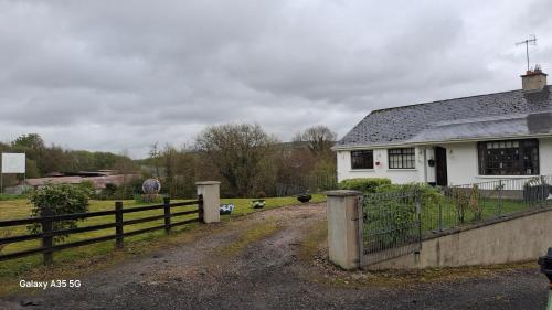 a white house with a fence next to a dirt road at Artisthostel Letterkenny in Letterkenny