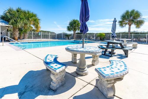 a table and benches with umbrellas next to a pool at Plantation East 2205 in Gulf Shores