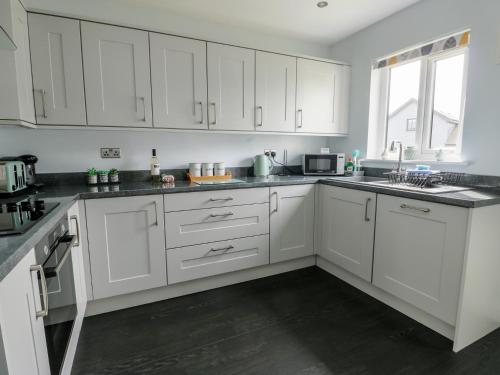a white kitchen with white cabinets and a window at 4 Parc Delfryn in Llanallgo