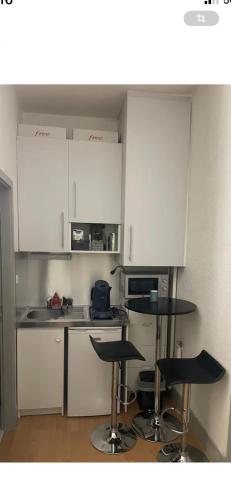 une cuisine avec des placards blancs et deux tabourets de bar dans l'établissement Appartement studio au cœur de Strasbourg, à Strasbourg