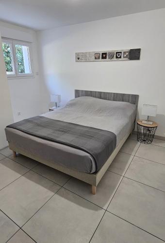 Ce lit se trouve dans une chambre blanche avec 2 tables. dans l'établissement Bas de villa, à Cavalaire-sur-Mer