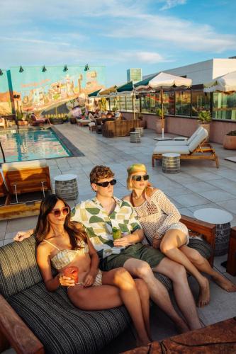 a group of three people sitting on a couch near a pool at HOLLYWOOD VOLUME, a Tribute Portfolio Hotel in Los Angeles