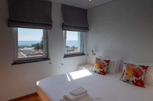 a bedroom with a white bed with two windows at Casa dos Remedios in Angra do Heroísmo