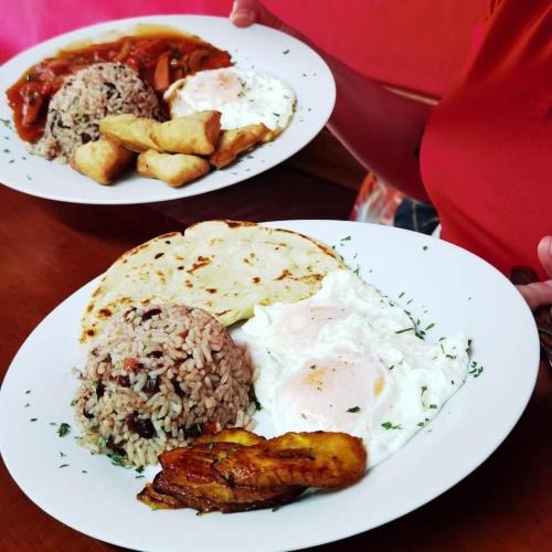 two plates of food with eggs meat and rice on a table at Hotel Costa del Sol in Puerto Limón