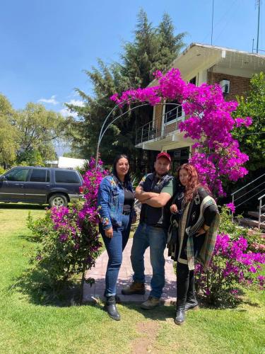 three people standing in front of a house with flowers at Telpochcalli Hotel & Temazcal in San Juan Teotihuacán