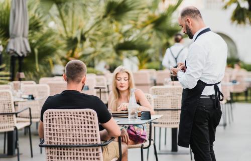 a man talking to a woman sitting at a table at Flower Hotels & Resorts in Golem