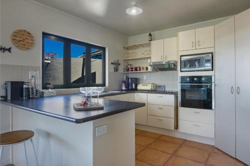 a kitchen with white cabinets and a black counter top at Virtue Escape - Beachside Bliss at Tokerau Beach in Kaitaia