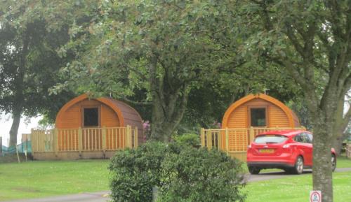 a red suv parked in front of two wooden buildings at Drumshademuir Caravan & Camping Park in Glamis