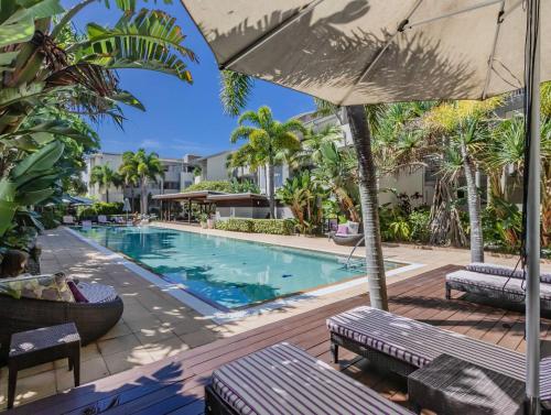 a pool at a resort with benches and an umbrella at Bali Luxury Resort - Holiday Management in Kingscliff