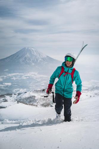 a man walking in the snow with skis on his back at Ginsetsu in Kutchan