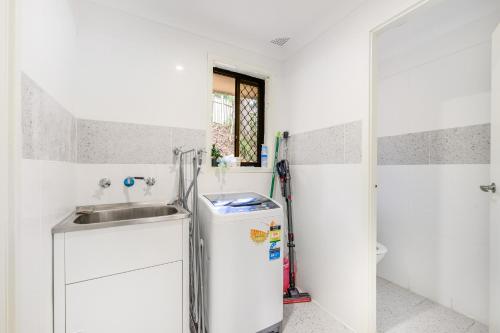 a white kitchen with a sink and a refrigerator at 5BR Peaceful Oasis with Wifi Garage in Hornsby