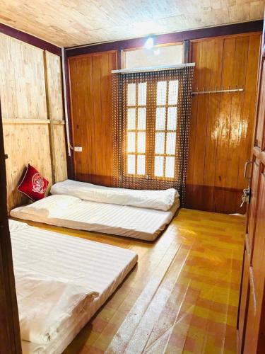 two beds in a room with wooden walls and a window at Cầu Treo Homestay in Cham Ta Lao