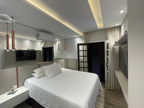 a bedroom with a white bed and a television at Paraiso na Praia da Enseda in Guarujá