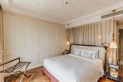 a bedroom with a large white bed and a chair at Hotel Des Arts Saigon Mgallery Collection in Ho Chi Minh City