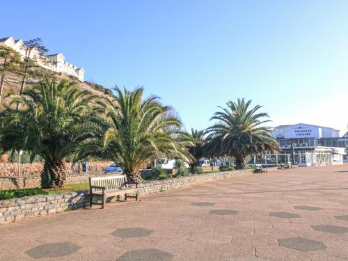 a park with palm trees and a bench and a building at Delmonte Lodge in Torquay