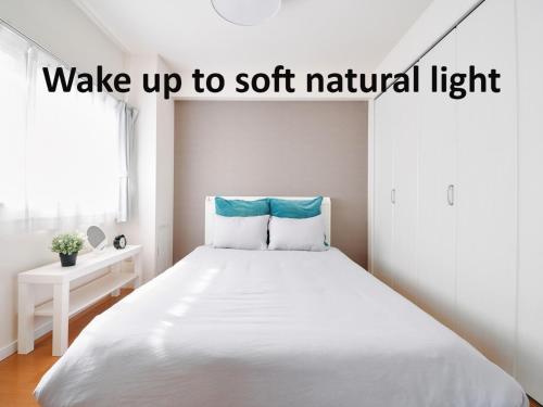 a bedroom with a large white bed with the words wake up to soft natural light at Nakano Apartment hotel in Tokyo