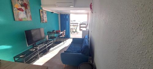 un salon avec un canapé bleu et une télévision dans l'établissement Appartement 78, PORT NATURE colline 2 au village naturiste, au Cap d'Agde