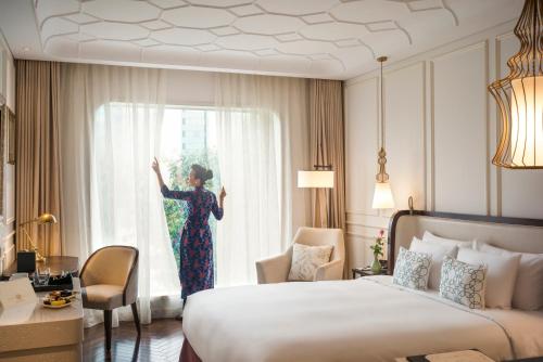 a woman is looking out the window of a hotel room at Hotel Des Arts Saigon Mgallery Collection in Ho Chi Minh City