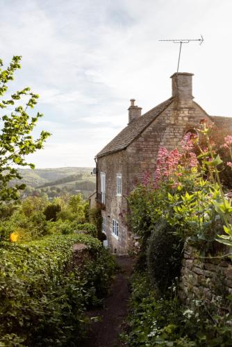 an old stone house with flowers in front of it at Painter's Cottage in the Cotswolds in Woodchester