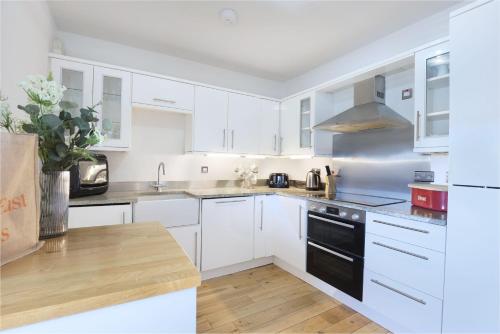 a kitchen with white cabinets and a black appliance at Stewards Cottage - North East Escapes in Bamburgh