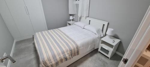 a small white bedroom with a bed and a night stand at Samsara apartment, esencia de mar in El Vendrell