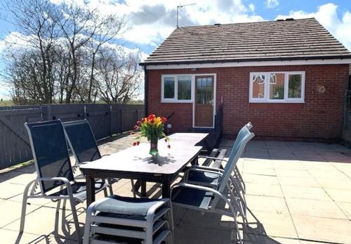 ein Tisch mit Stühlen und einer Vase mit Blumen auf einer Terrasse in der Unterkunft Primrose Valley Bungalow in Filey