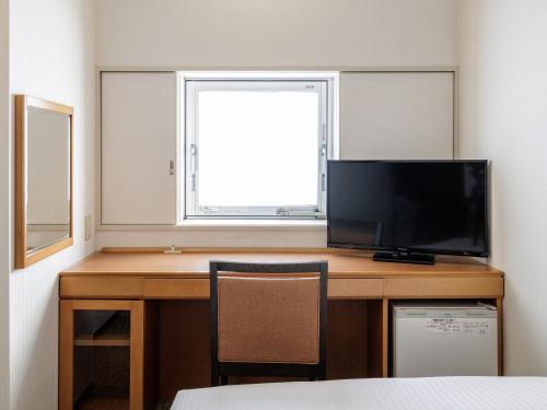 a room with a desk with a television and a window at Nishitetsu Inn Kurosaki in Kitakyushu