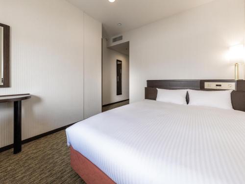 a bedroom with a large white bed and a desk at Nishitetsu Inn Kurosaki in Kitakyushu
