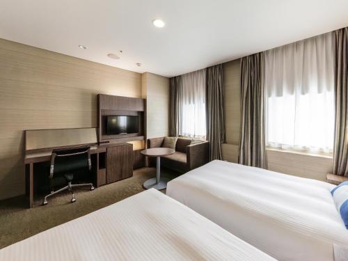 a hotel room with two beds and a desk at Nishitetsu Inn Kurosaki in Kitakyushu